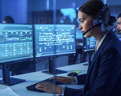 Lady with receptionist headset seated and working at a dual monitor computer setup