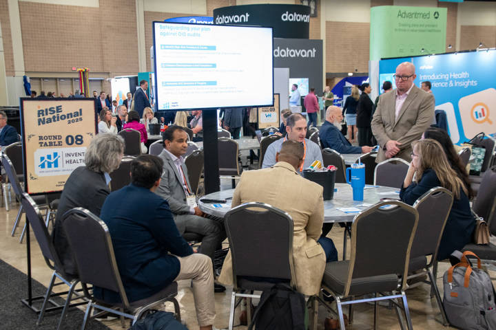 Numerous individuals gathered around tables in conference hall