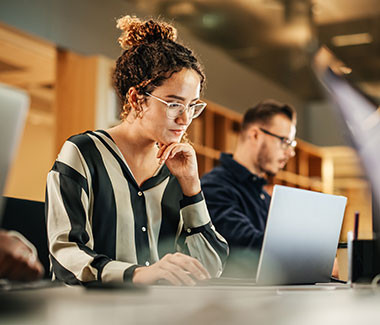 A woman and a man looking at their respective laptops