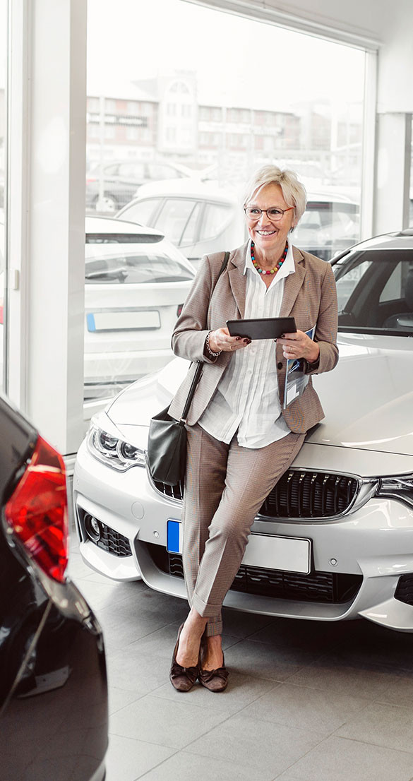 saleswoman leaning on vehicle at auto dealer using a tablet
