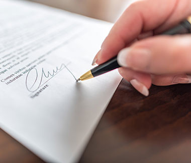 Primer plano de la mano de una mujer sosteniendo un bolígrafo y firmando en un papel.