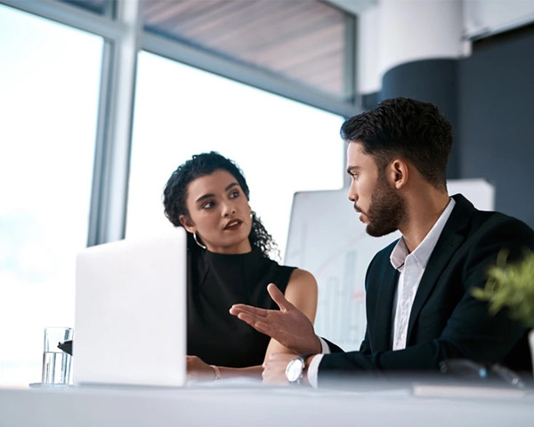 A person explaining something to another person sitting in front of a laptop