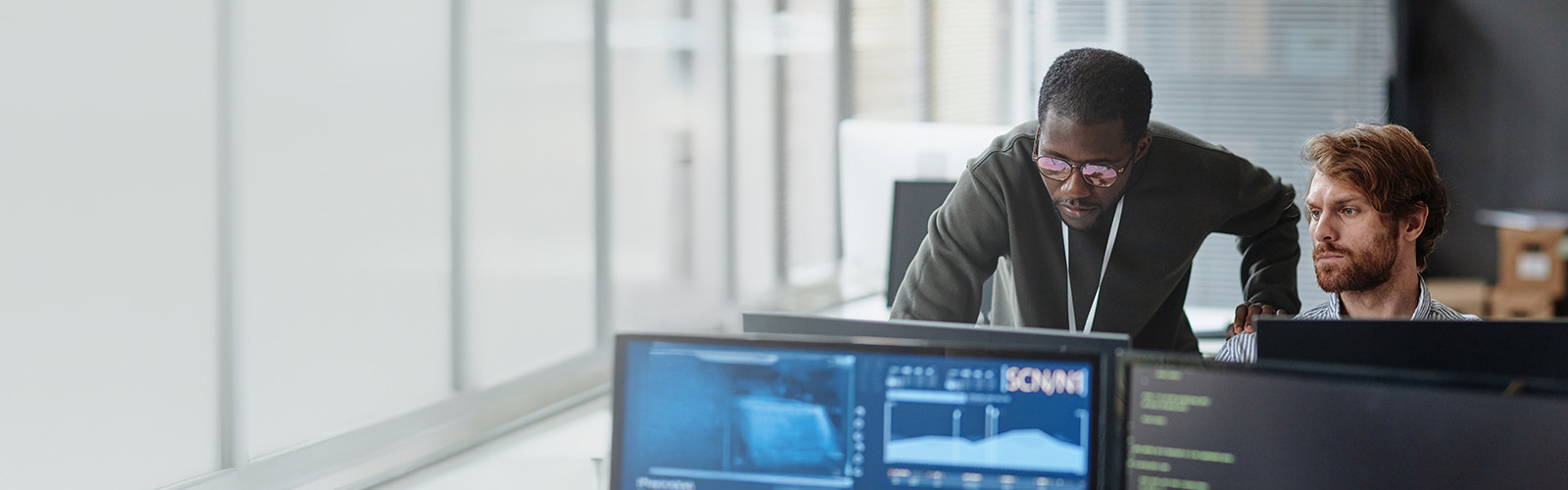 Two colleagues working together at computer monitors in an office