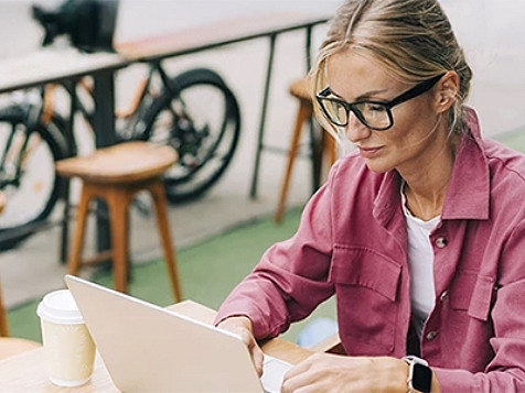 A woman seated at a table, focused on her laptop, engaged in work.