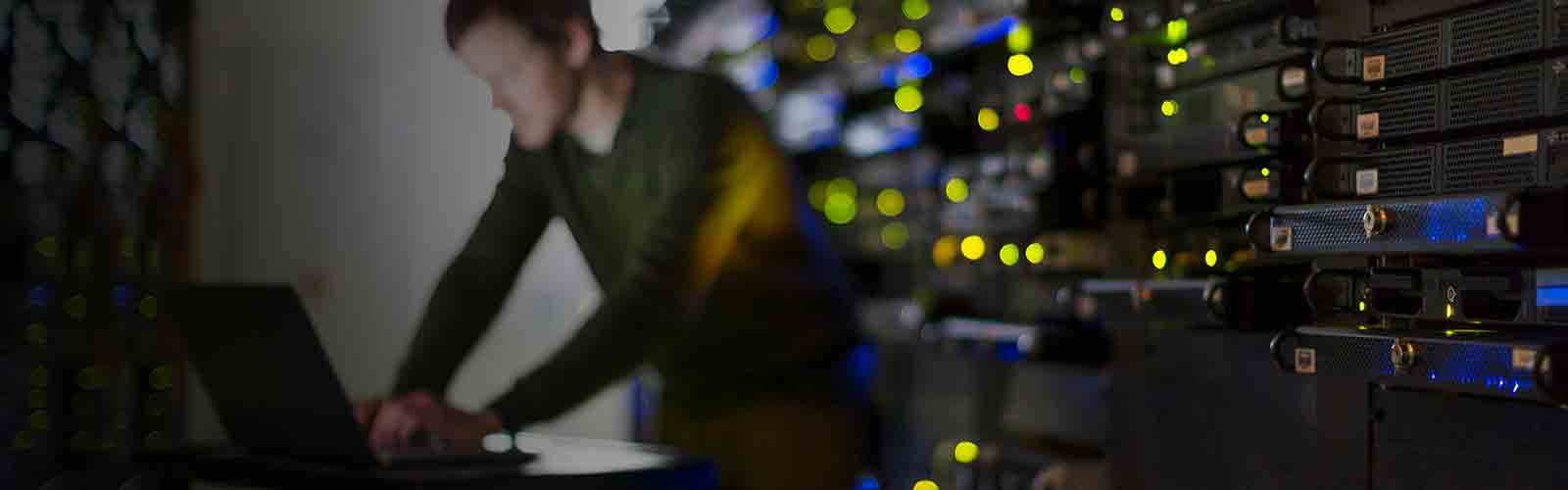 Blurred image of man working on a laptop in a server room