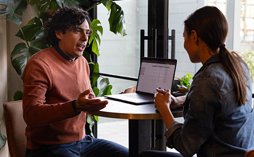 två personer samtalar framför en bärbar dator