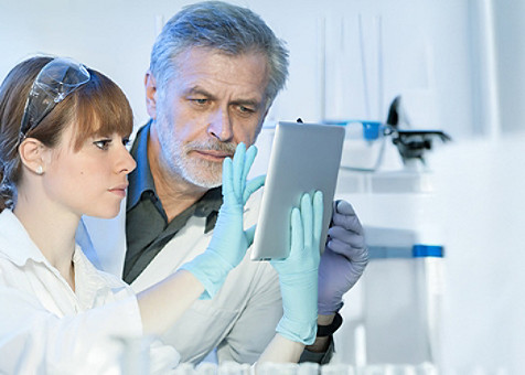 A lab technician interacting with a tablet as her colleague looks into it