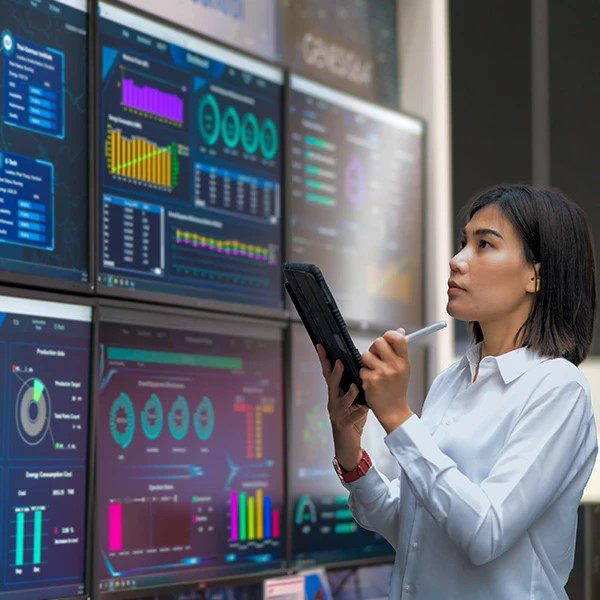 Lady standing, facing six computer monitor screens while working on a tablet