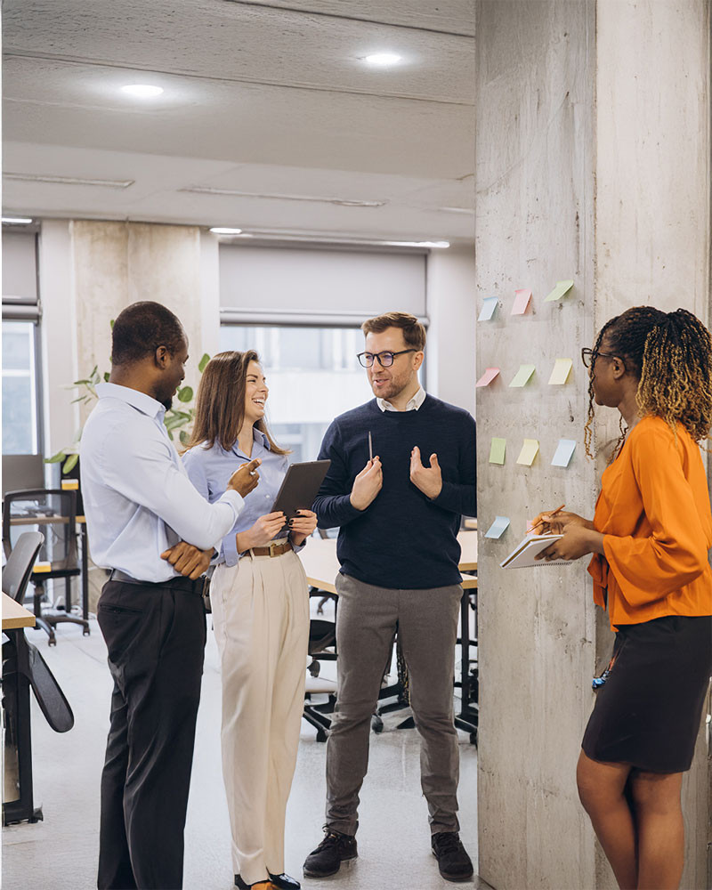 Three diverse colleagues standing in a modern office, engaged in a conversation.