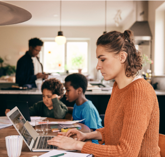 Femme travaillant depuis chez elle avec ses enfants et son partenaire en arrière-plan