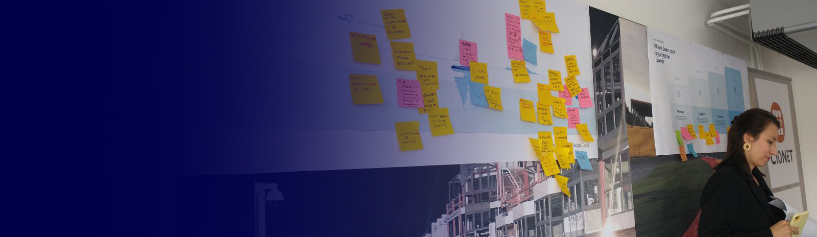 A lady standing at an event next to a white board with sticky notes.