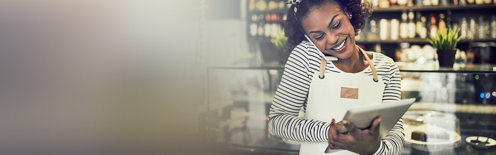 A woman smiling and talking on a phone while holding a tablet in hand