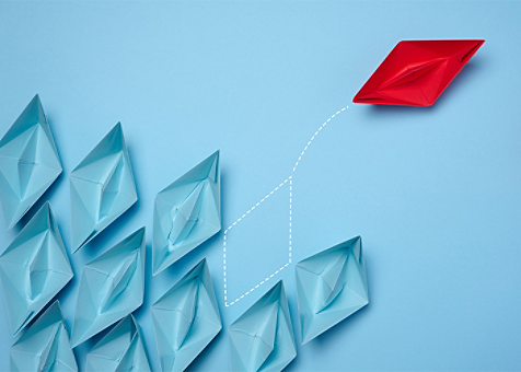 a red paper boat moving in opposite direction of a group of blue paper boats