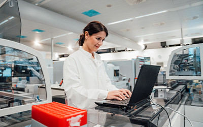 Laboratory professional using a laptop in an advanced scientific manufacturing and testing environment.