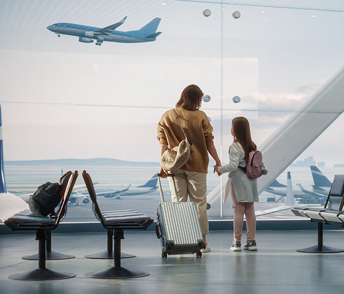 A mother and daughter looking at a flight taking off from inside an airport