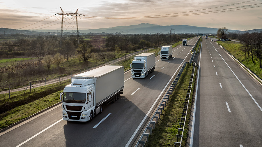 Freight trucks traveling on a highway through a rural area.