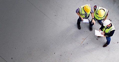 Three workers wearing helmets and hazard jackets having a discussion