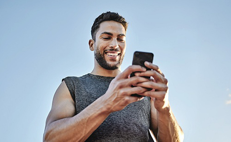 Male in grey sports top looking at mobile phone, smiling.