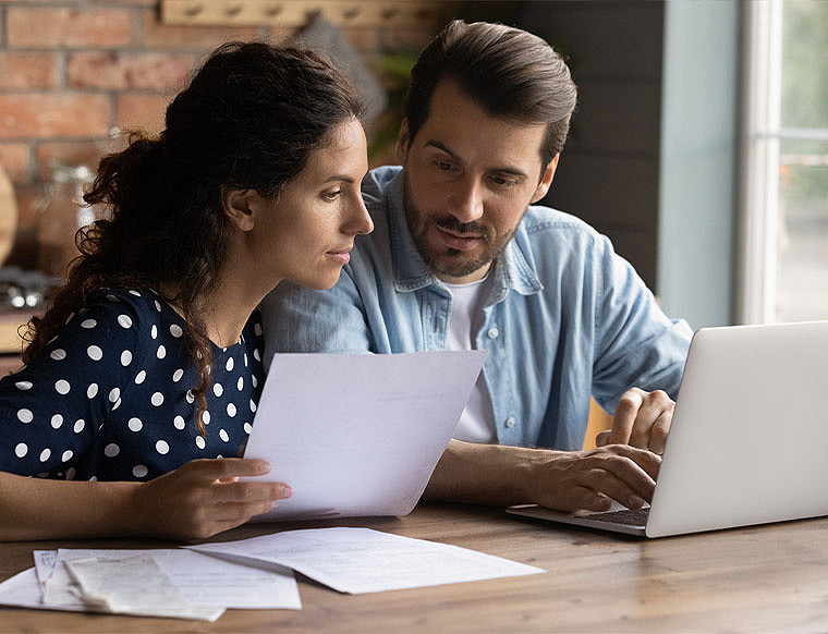 A man and woman discussing something in fornt of the laptop by keeping a paper in hand