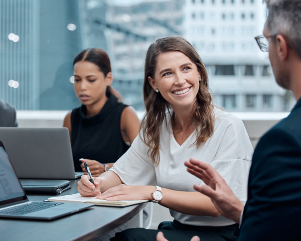 Lady smiling infront of laptop and listening to another person.
