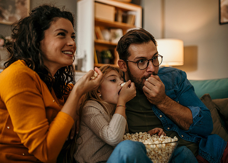 A family of three eating pop corn and watching TV