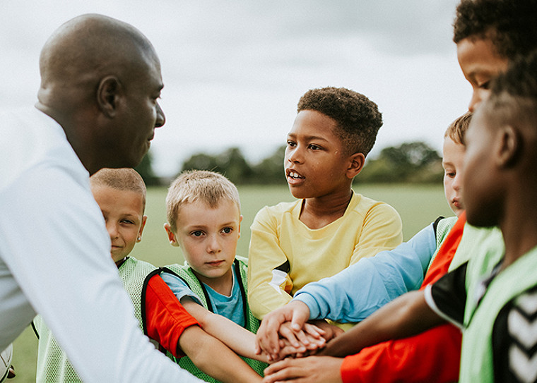 Kids doing a huddle with the coach on a football field