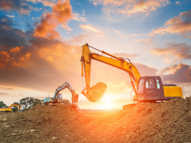 A bulldozer working in an open field with the sun behind it.