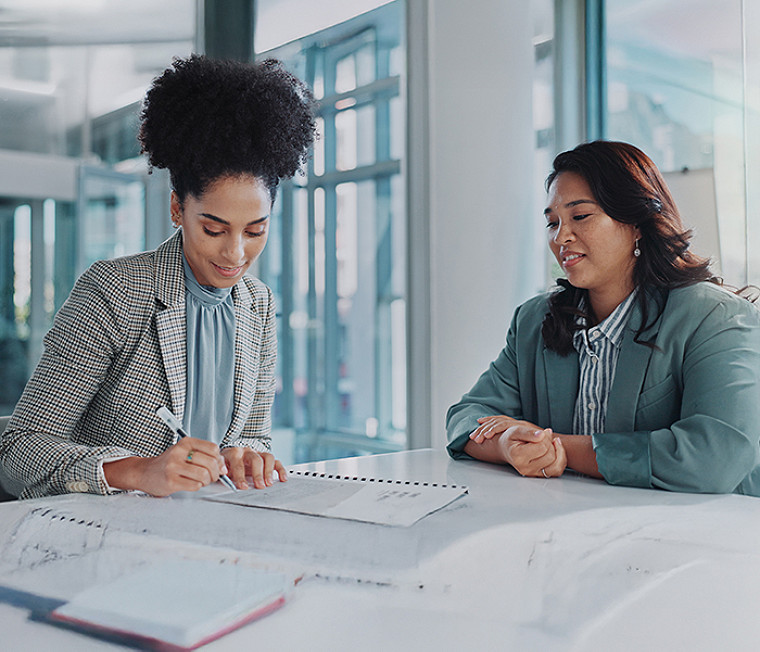 Two colleagues sitting on a table and discussing while one takes a note