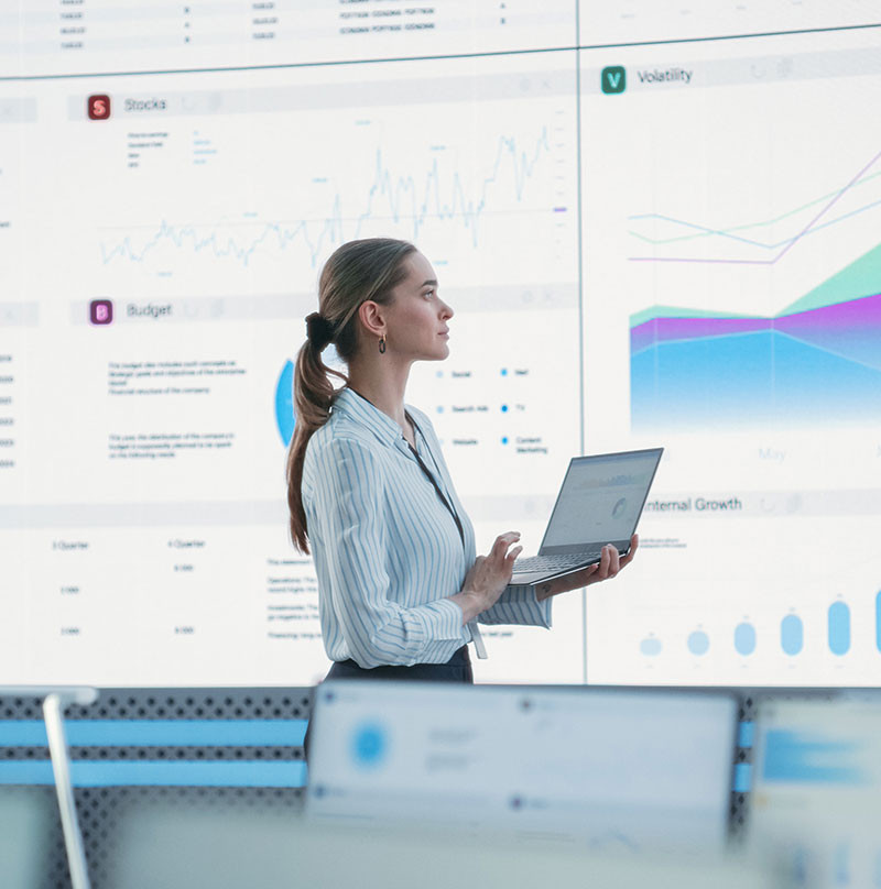 A young female business professional looking large screen displaying data analytics dashboards