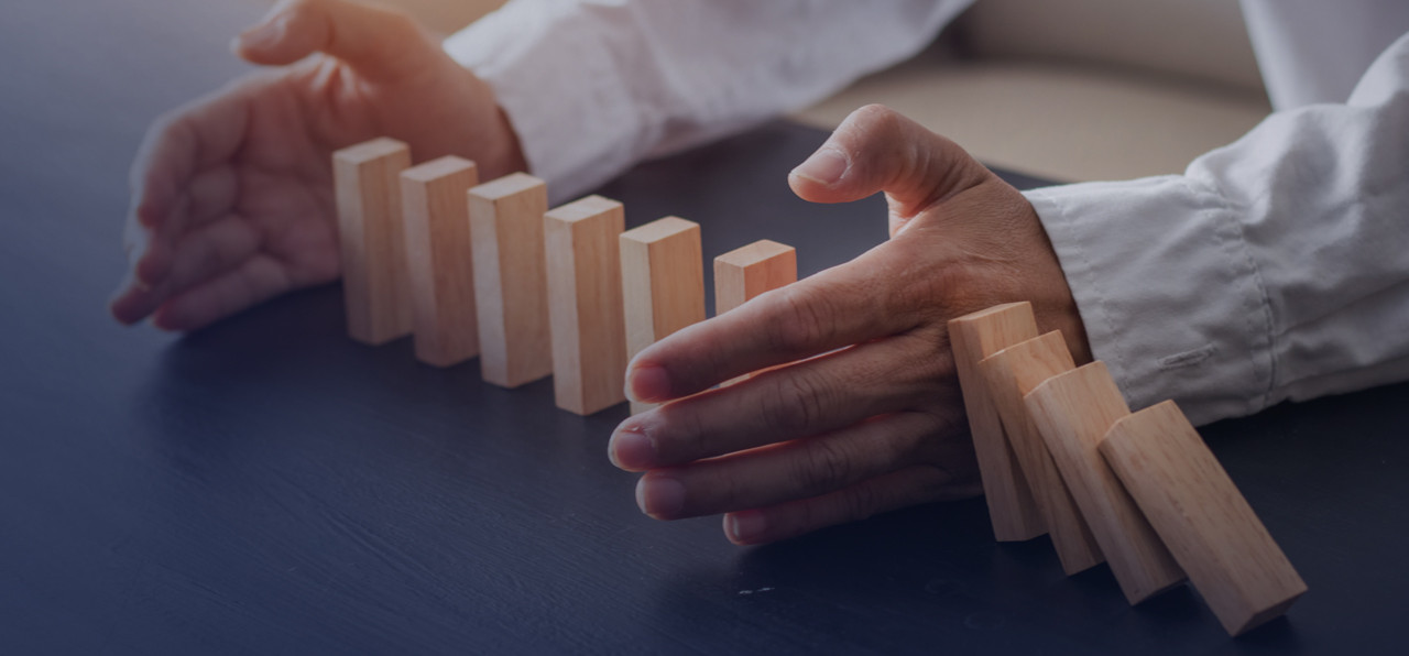 Man's hand in the middle of wood dominos standing up on one side and falling down on the other side