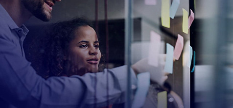 A Man and an women sticking the sticky notes to the glass wall.