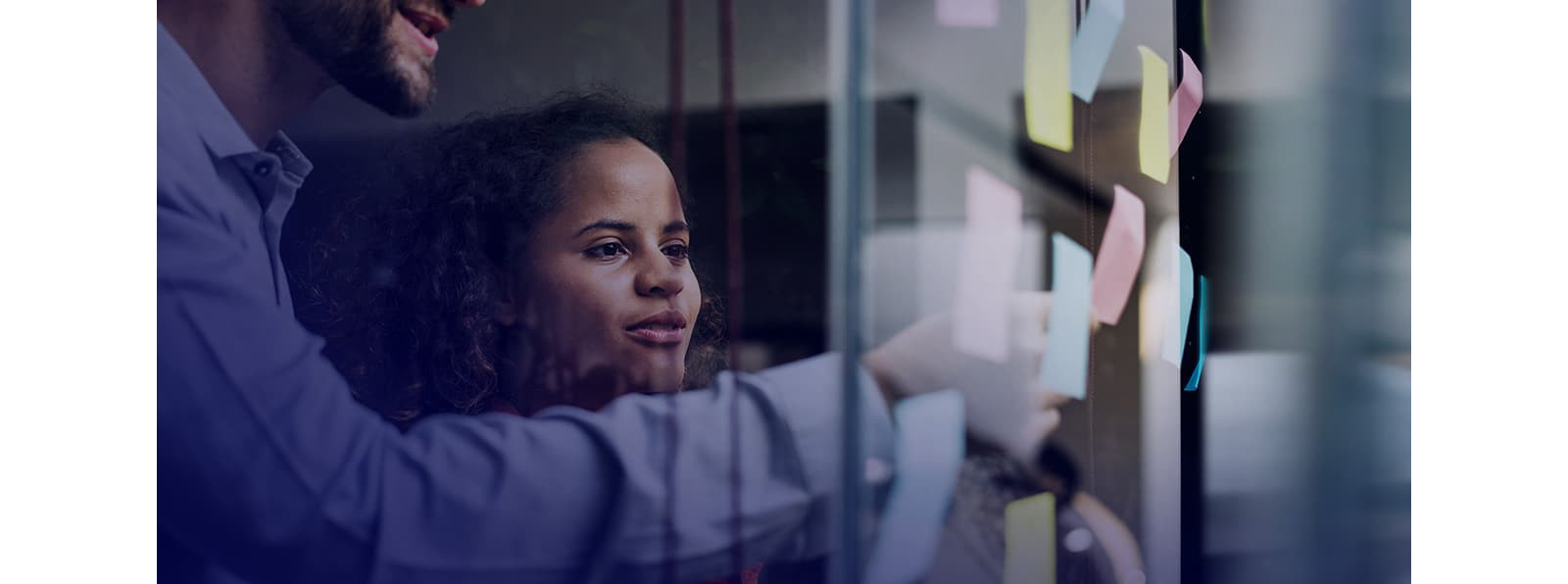 A man and woman pasting sticky notes on a glass wall