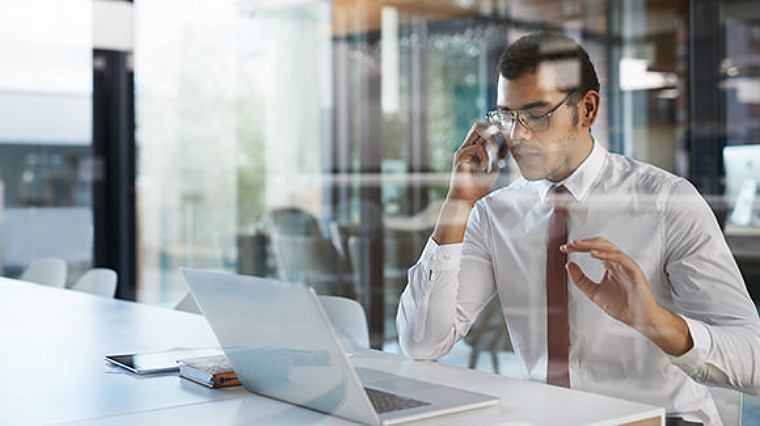 Homme parlant au téléphone devant un ordinateur portable