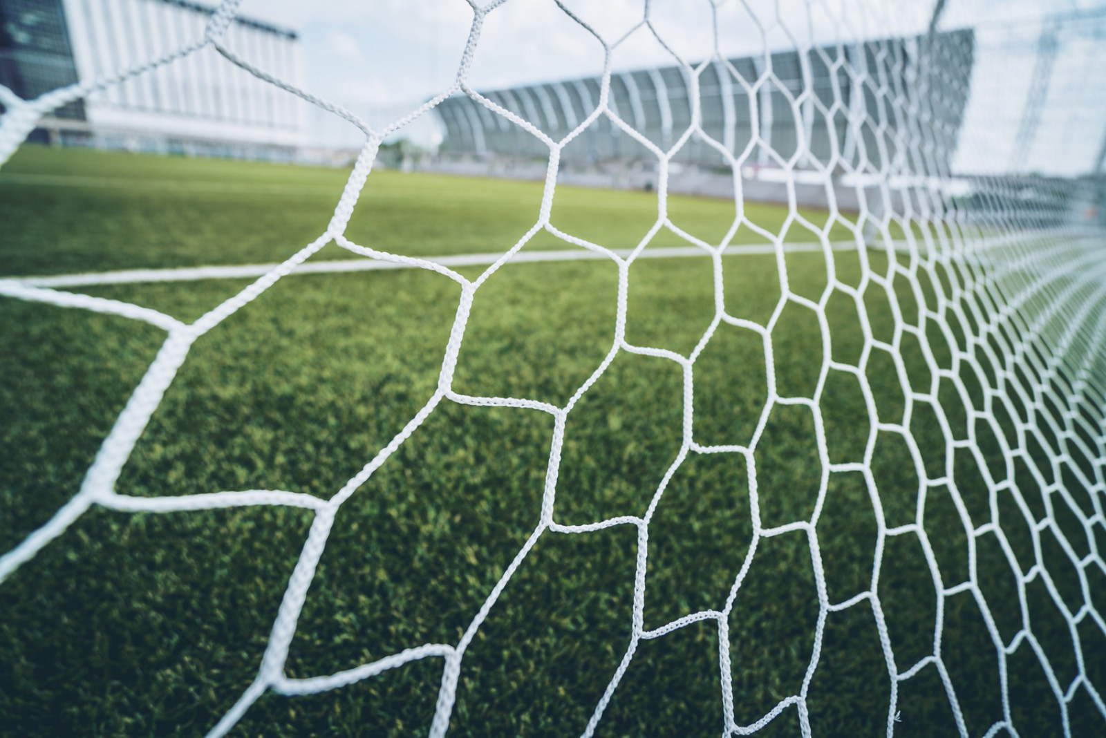 Soccer football net background over green grass and blurry stadium behind