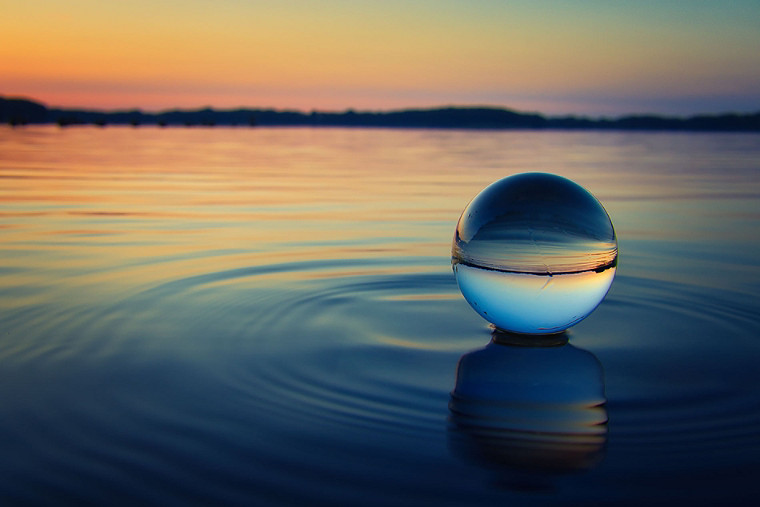 A large waterdrop over a pool of water with the sunset in background.