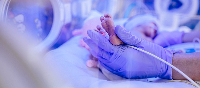 Holding a newborn's foot in an incubator