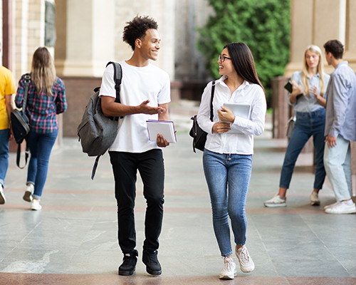 Zwei Studenten unterhalten sich unterwegs mit ihren Taschen und Büchern in der Hand