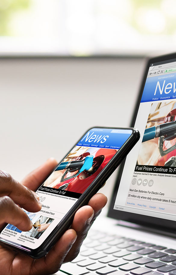 Hand holding cellphone device showing news on screen with monitor in background