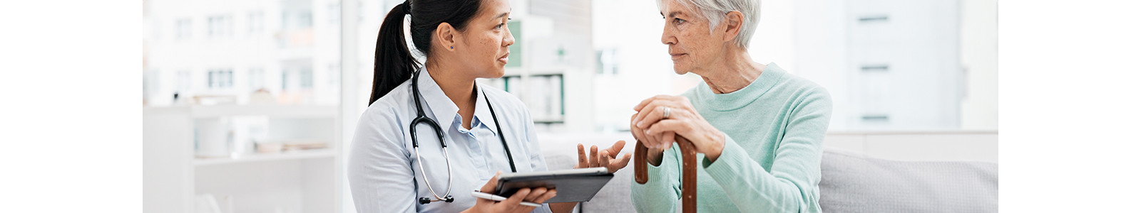 A doctor holding a tablet talks to an elderly patient with in room.