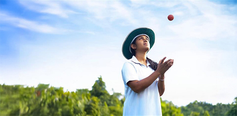 A cricket player tossing the cricket ball in the air.