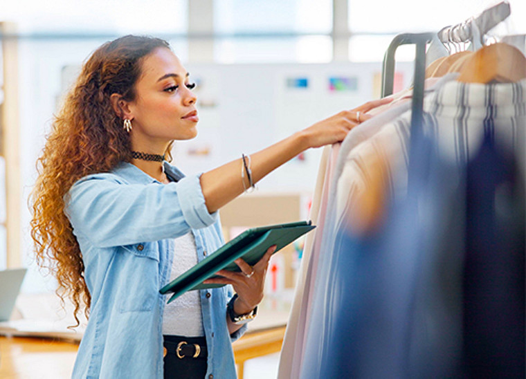 A young woman checking out some clothes on a hanger while holding a tablet in one hand.