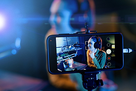 Young woman streaming a live video with her smartphone and talking into a microphone in the studio