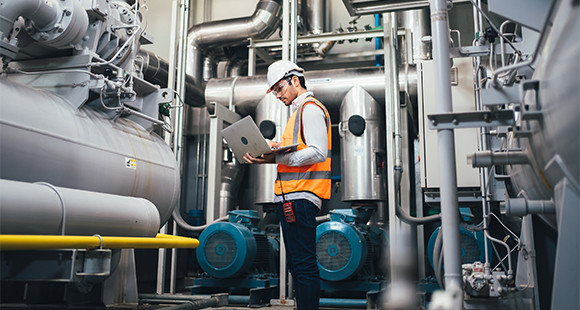 A male employee in a boiler room looking at laptop screen 