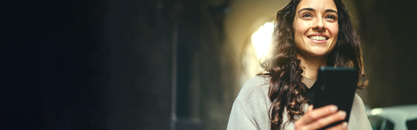 Young woman holding a phone and looking ahead and smiling.  