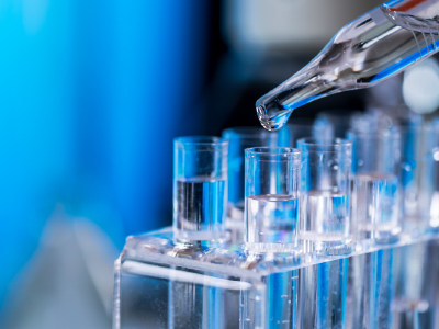 Test tubes with liquid solution in a holder and a dropper hovering on one dispensing more solution