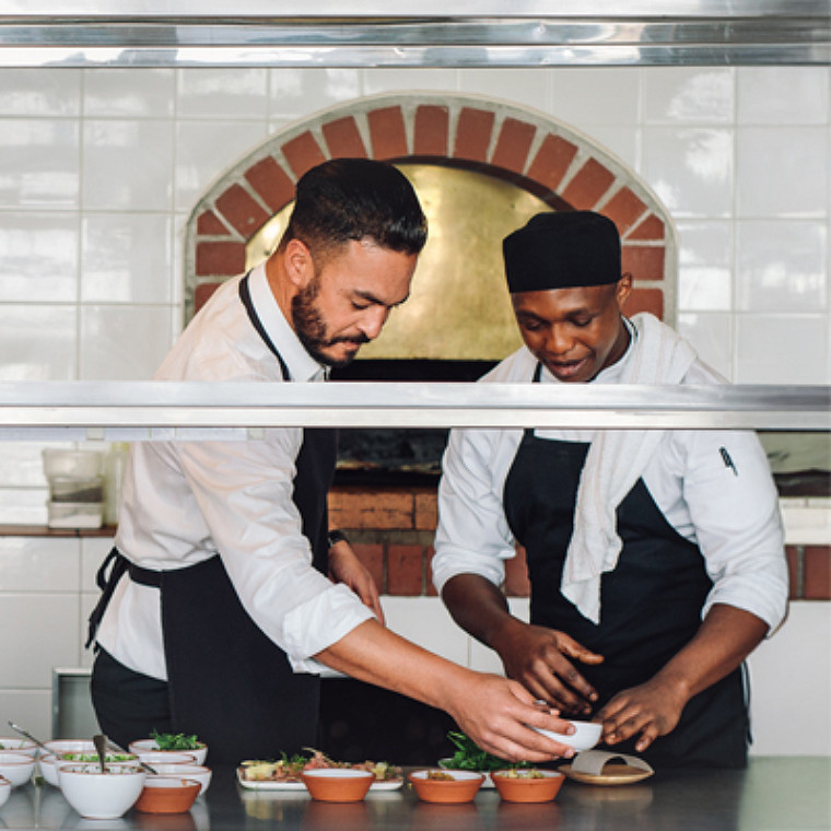 Two male chef colleagues working on a dish together.