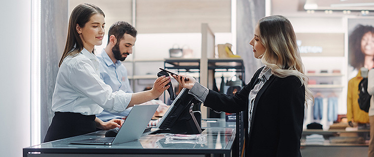 A customer at the checkout counter in a retail store handing a mobile phone to the cashier