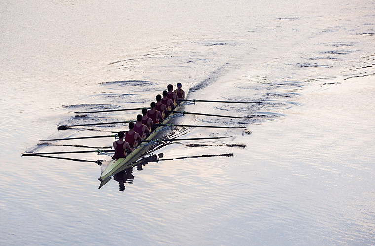 Rowing team rowing scull on lake