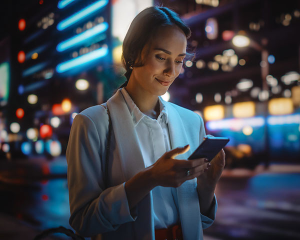 Une femme avec un téléphone mobile à la main dans la rue, en soirée.