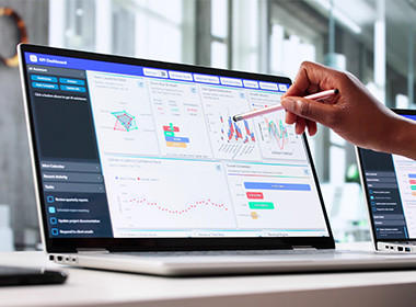 Hand using stylus on laptop with analytics dashboards